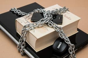 Laptop, książka i telefon spięte grubym łańcuchem symbolizując cenzurę